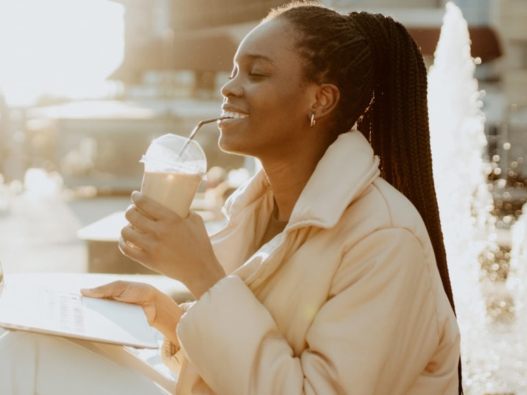 woman drinking iced coffee in front of open laptop