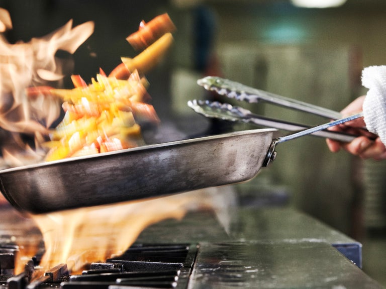 chef holding pan over open flame