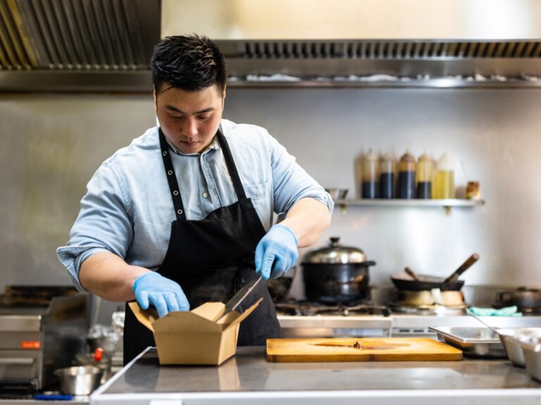 chef in kitchen adding food to a take out container