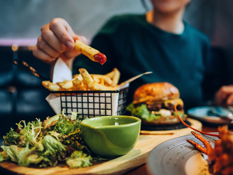 Man holding a french fry dipped in ketchup with broccoli on wooden board