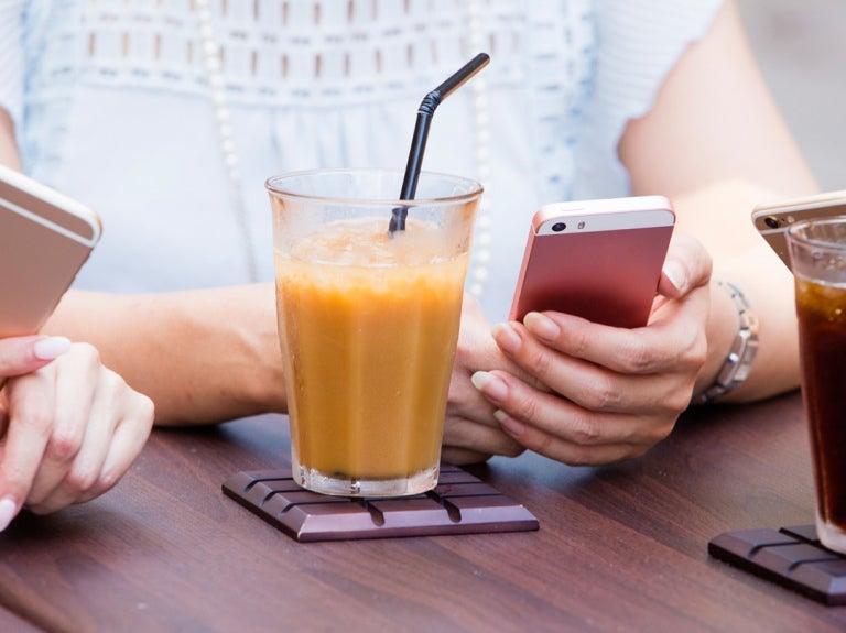 women sitting at table with juice in glass holding cell phones