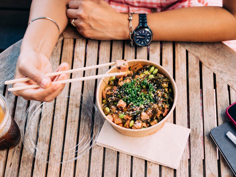 person at table using chopsticks to eat an entree in a bowl