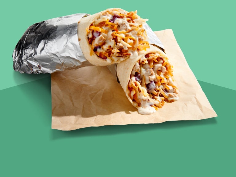 burrito in foil cut in half laying on a paper napkin with green background