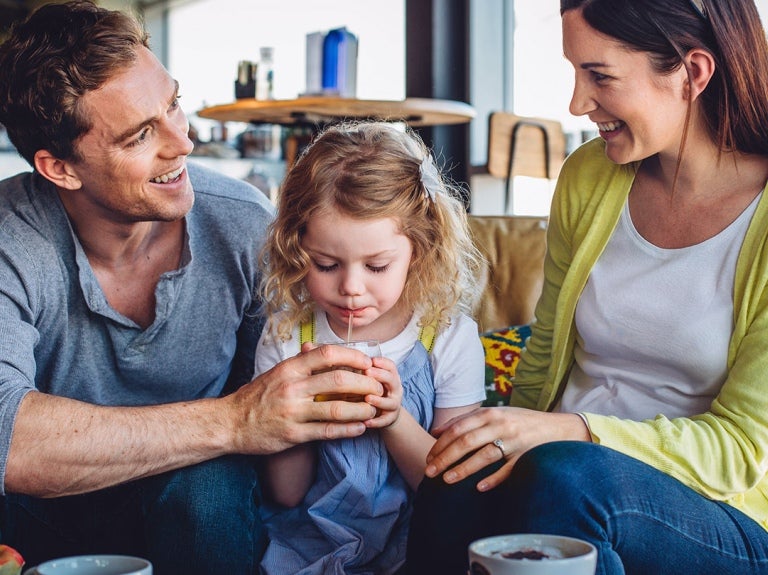 man and woman sitting on couch with girl drinking beverage from straw