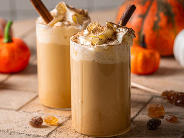 two pumpkin lattes with straws and pumpkins in background