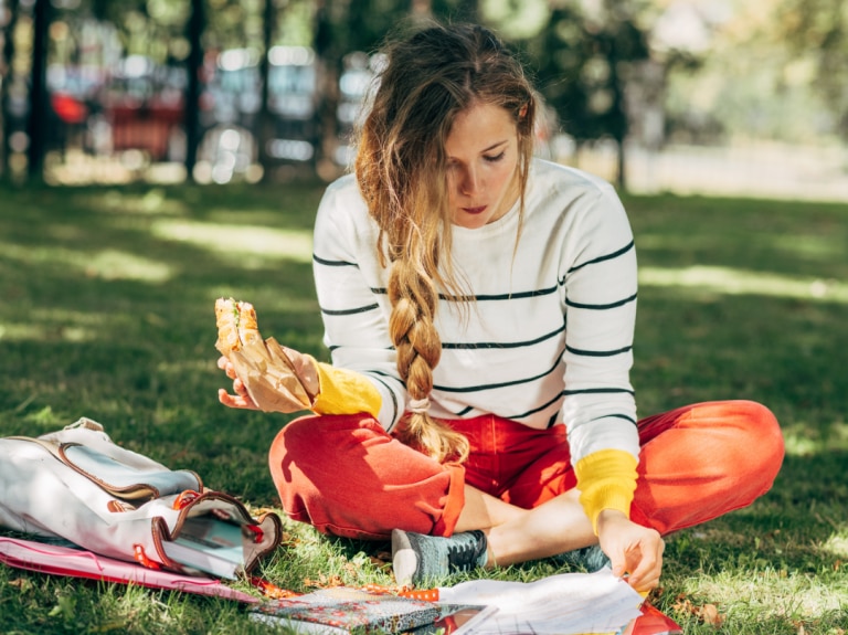 woman sitting on grass eating sandwich while reading