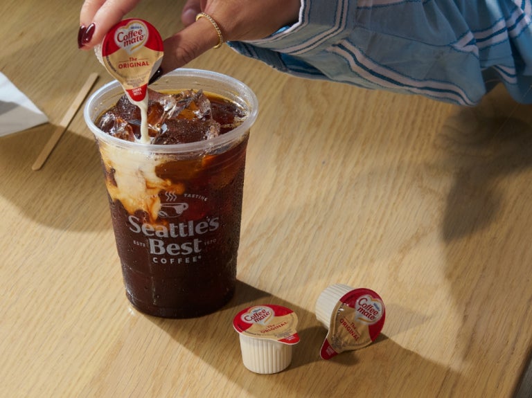 adding coffee mate creamer singles into a cup of iced coffee