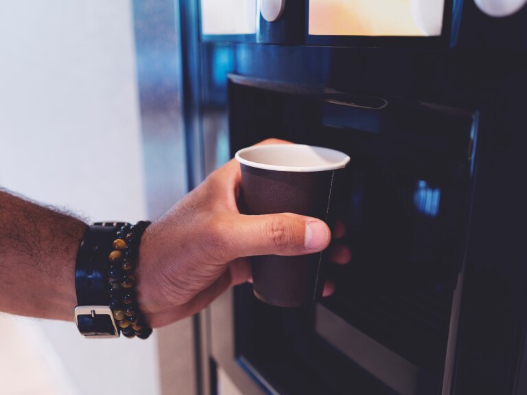 person filling a cup of coffee from machine