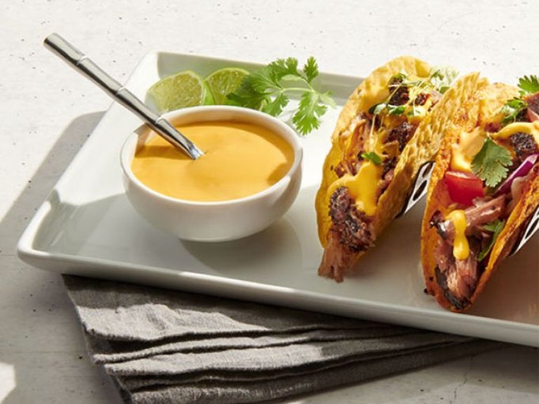cheese sauce in bowl on plate with two tacos