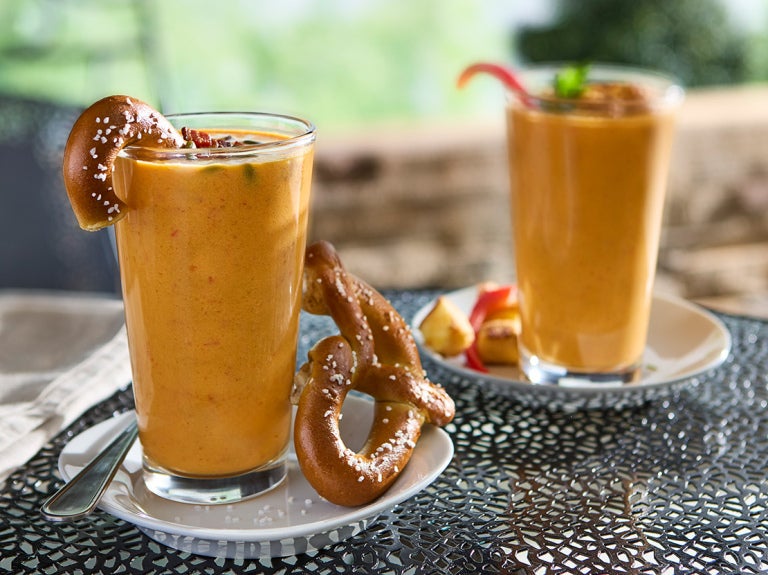 Two pumpkin-colored smoothies in tall glasses, one served with a large soft pretzel.