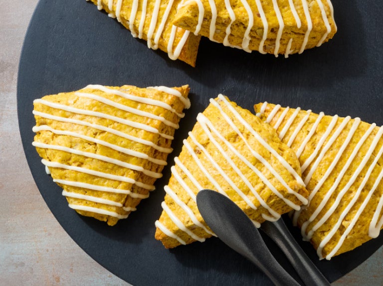 A plate of frosted pumpkin scones with tongs picking one up