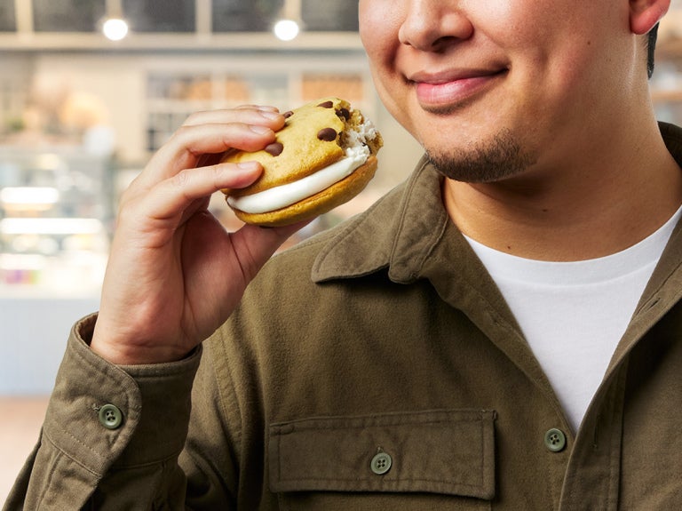 Close up of a man with a big smile holding a cream-stuffed whoopie pie up to his mouth.