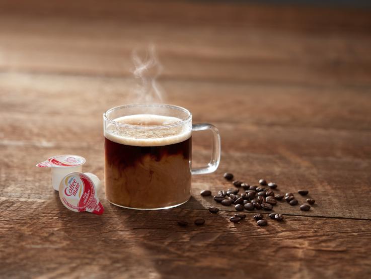 Nescafe Americano coffee drink in clear glass mug and 2 tubs of Coffee mate creamer next to it