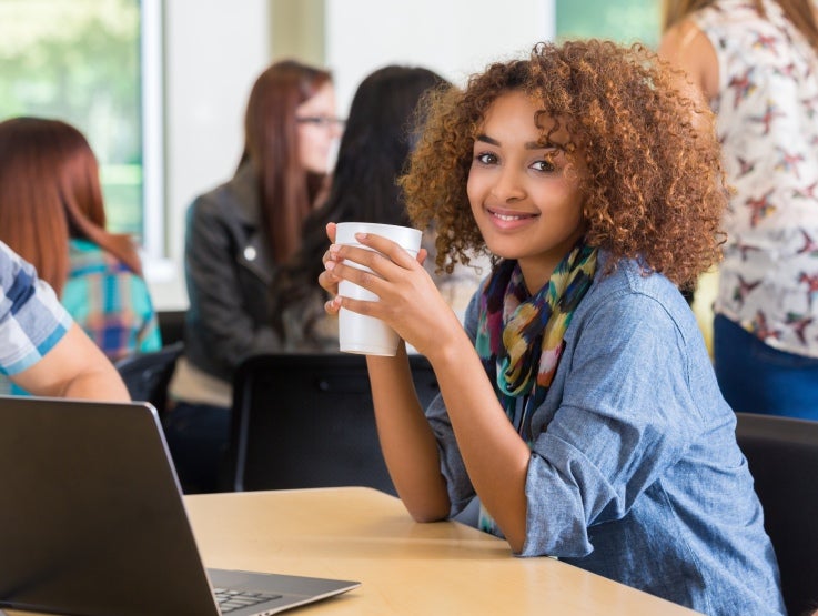 Woman holding a coffee cup sitting in front of computer