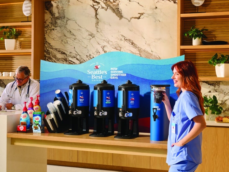 healthcare worker holding coffee while standing in from of coffee machines