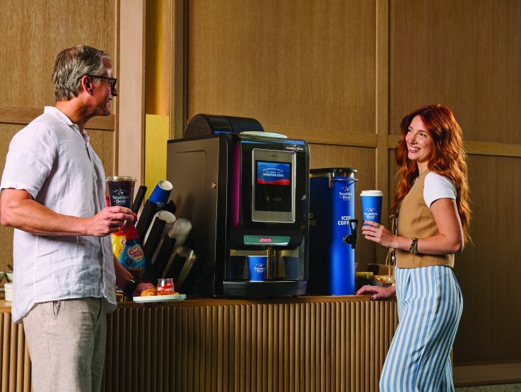 man and woman standing by coffee machine with coffee in hand