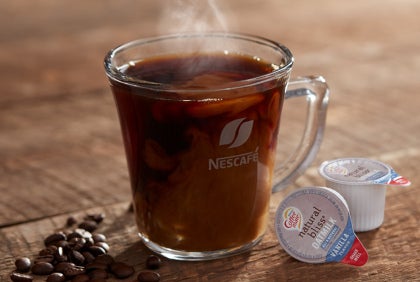 Cup of hot coffee with CoffeeMate oat-milk creamer pods on the side