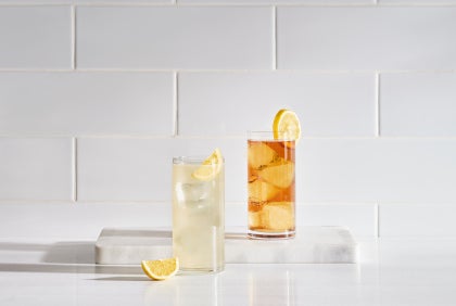 glass of lemonade and iced tea with slice of lemon and lemon wedge