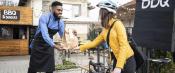 Man wearing apron handing BBQ takeout to a woman on a bicycle