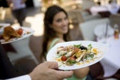 Close-up of 2 appetizers on white plates with a blurred woman in the background