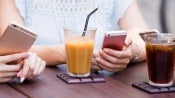 women sitting at table with juice in glass holding cell phones