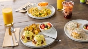 breakfast foods eggs, potatoes and fruit on table with iced coffee and orange juice